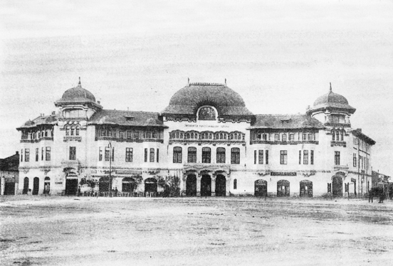 Historisches Schwarz-Weiß-Foto eines prächtigen, verschnörkelten Gebäudes mit drei großen Kuppeln und Rundbogenfenstern, mit kunstvollen architektonischen Details und einem weitläufigen Bereich vor dem Gebäude.