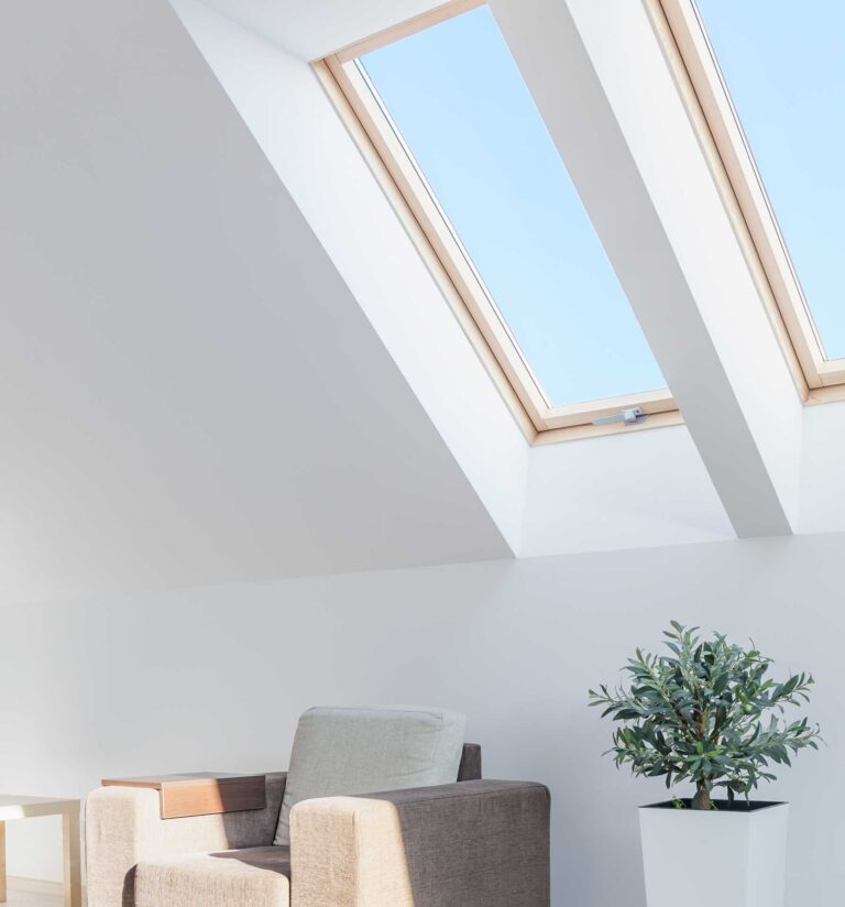 Ein modernes, minimalistisches Zimmer mit einem beigen Sessel, einem kleinen Beistelltisch, einer Topfpflanze und zwei großen Dachfenstern, die viel Tageslicht hereinlassen.